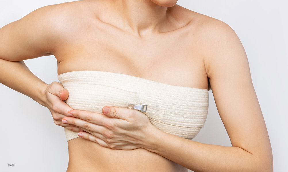 Close-up photo of a woman with bandages around her breasts and her hands cupping the bottom of her right breast.